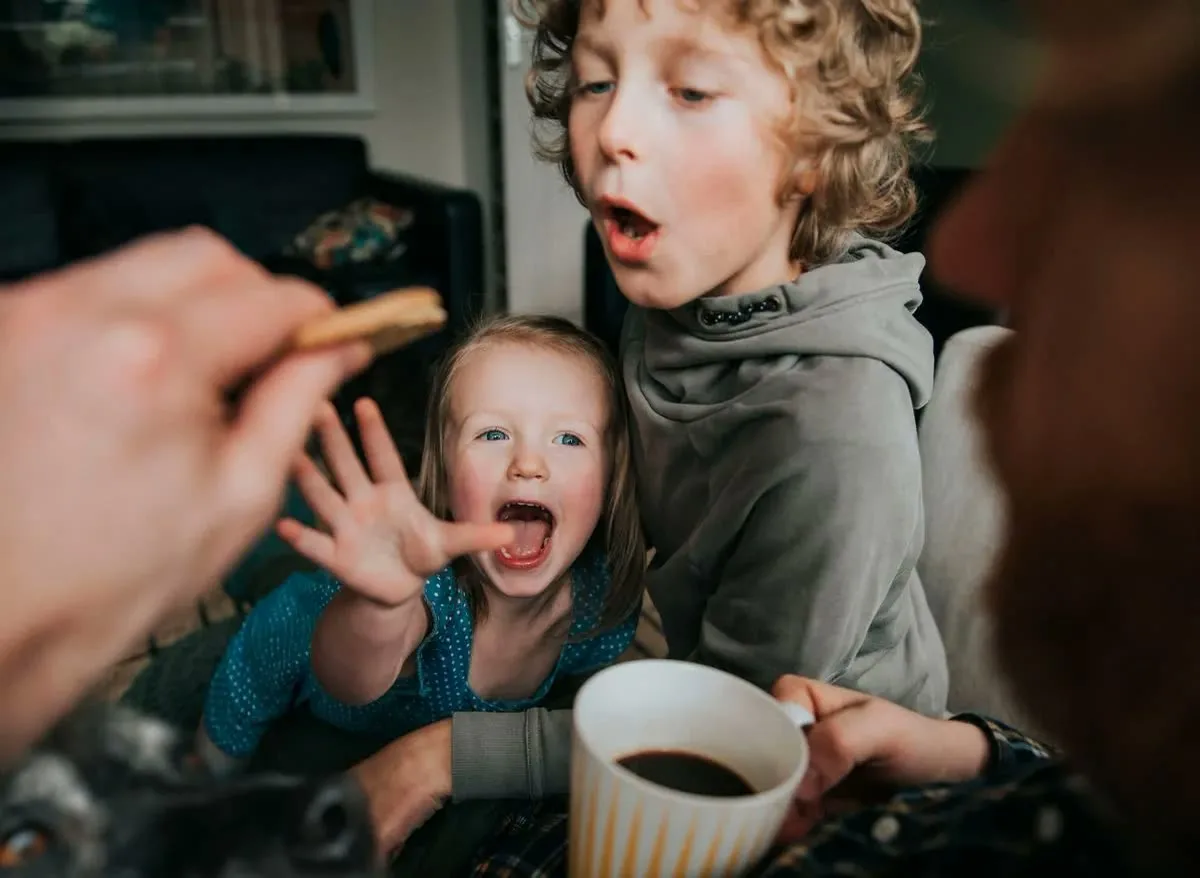 A toddler reaches for a biscuit, a mug of coffee in the foreground